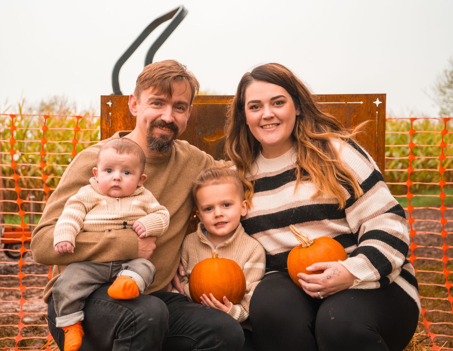 Family sitting together on wooden benches with pumpkin patch decor in background.