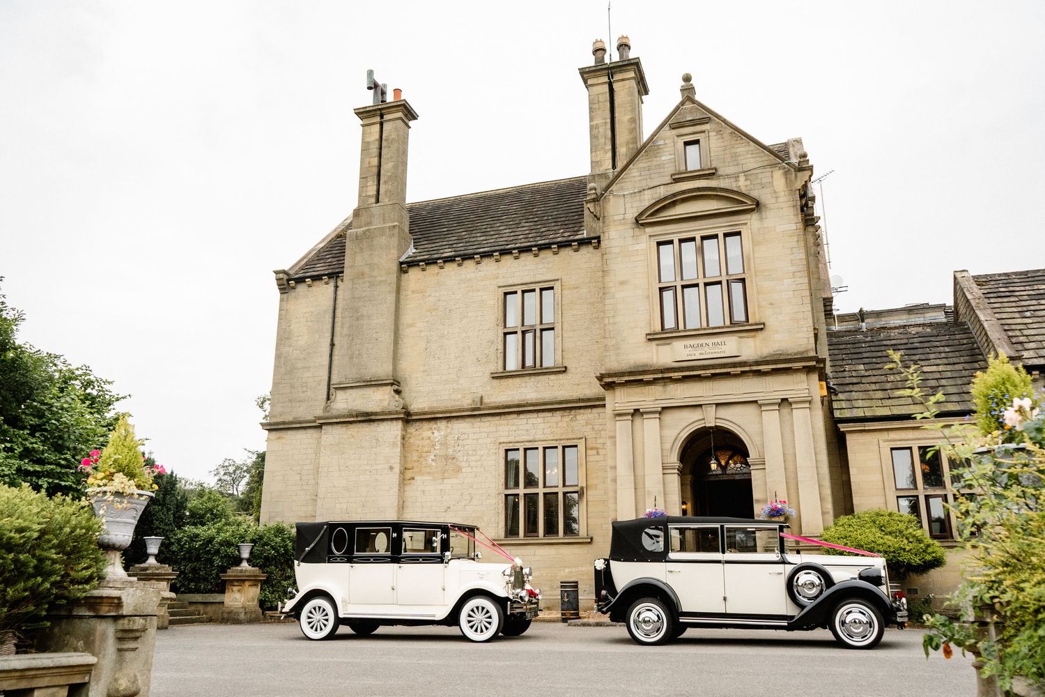 Classic vintage wedding cars parked outside a grand stone manor house.