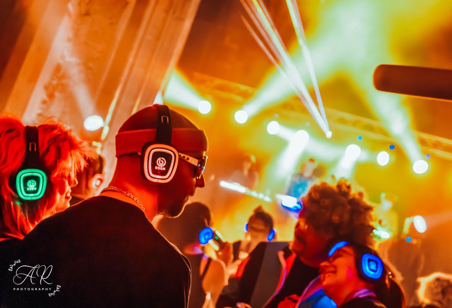 Dynamic light show with orange and blue beams illuminating a packed dance floor.