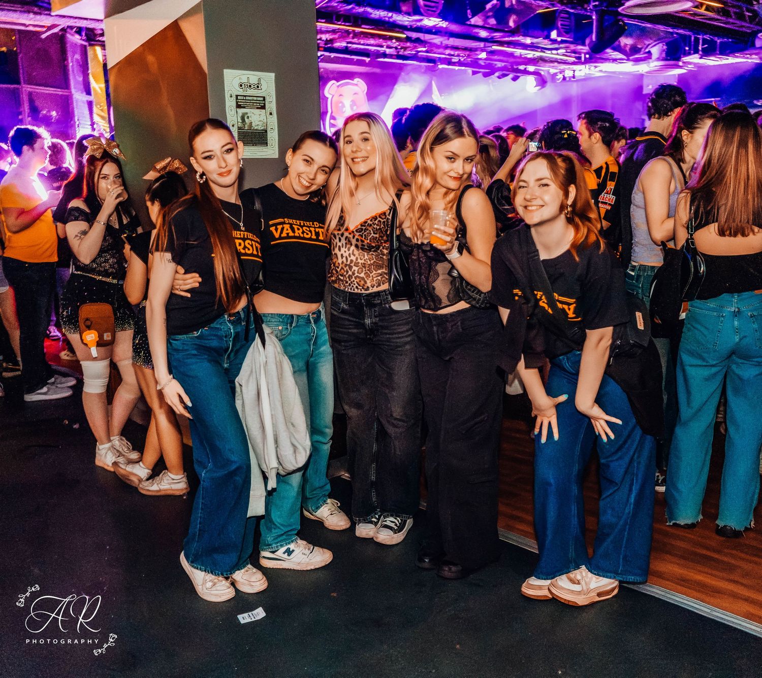 Group of friends in matching outfits enjoying a night out at a club with purple lighting and party atmosphere.