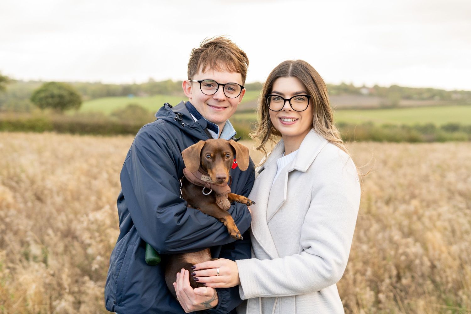 Family portrait with chocolate lab puppy in autumn field setting.