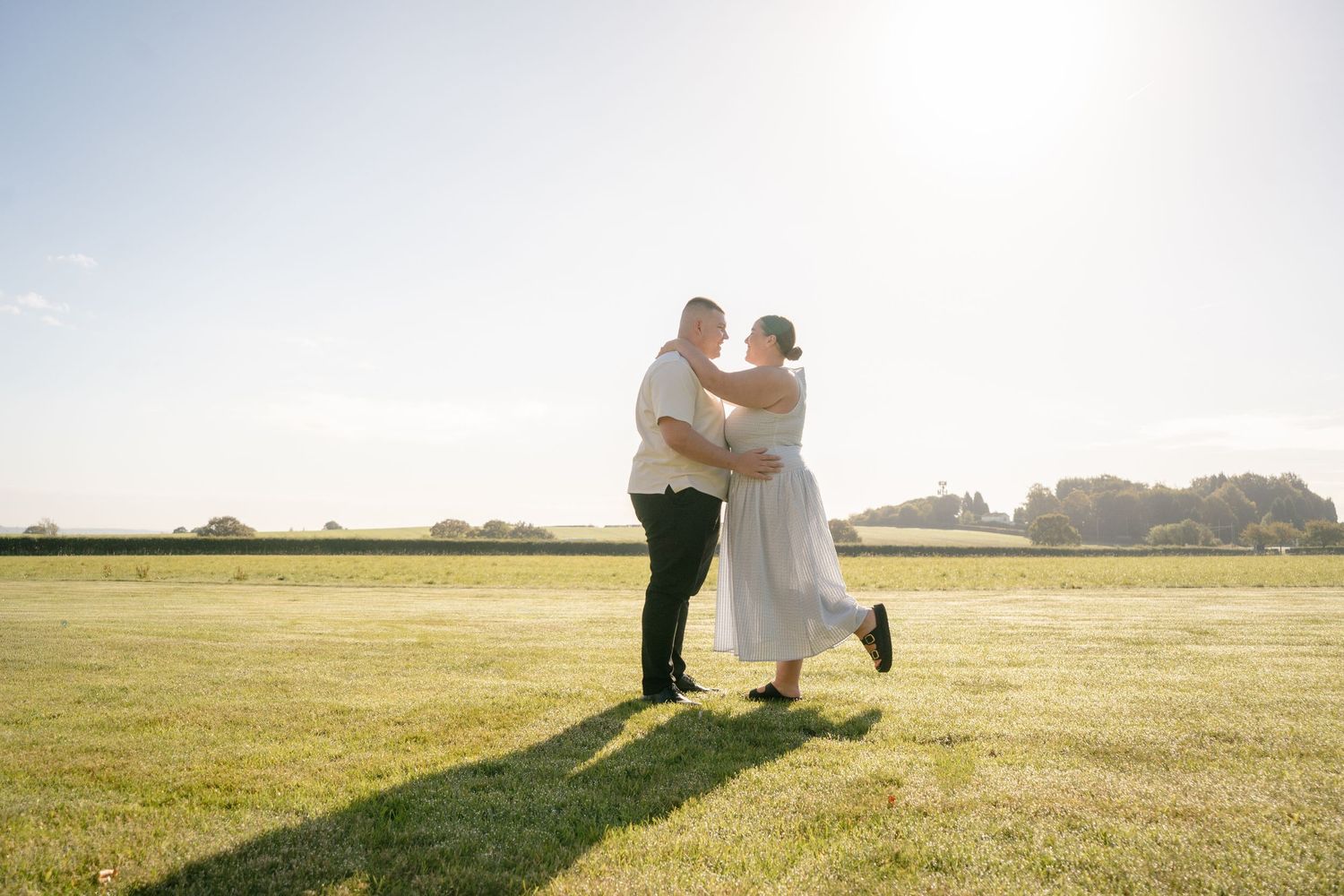 Romantic couple dancing together in an open field at sunset.