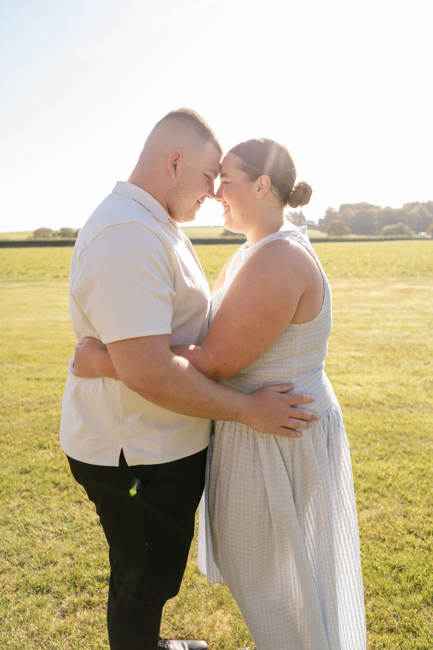 A couple in white and black attire embraces in a sunny meadow.