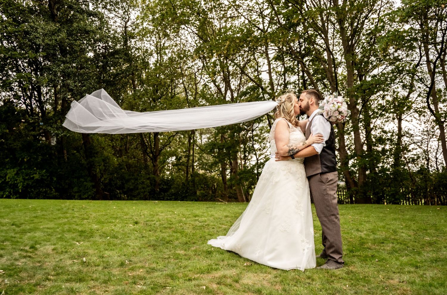 Wedding couple embracing in an outdoor garden setting with a dramatic flowing veil.