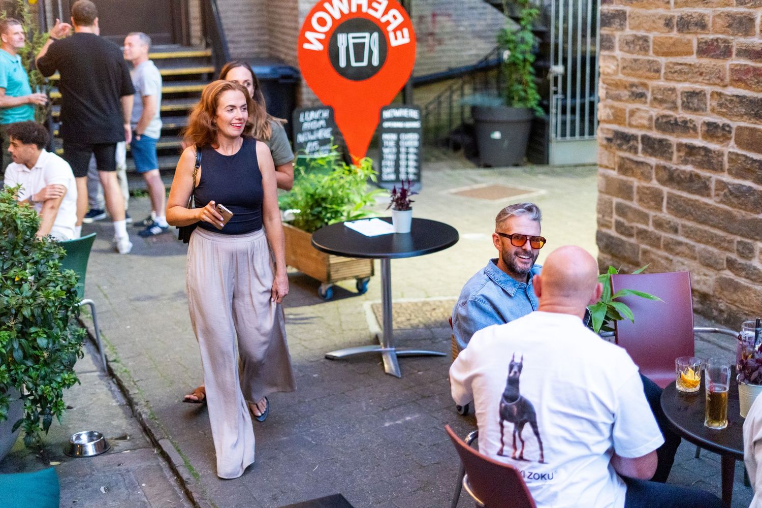 People mingling outside a bar patio area with brick walls.