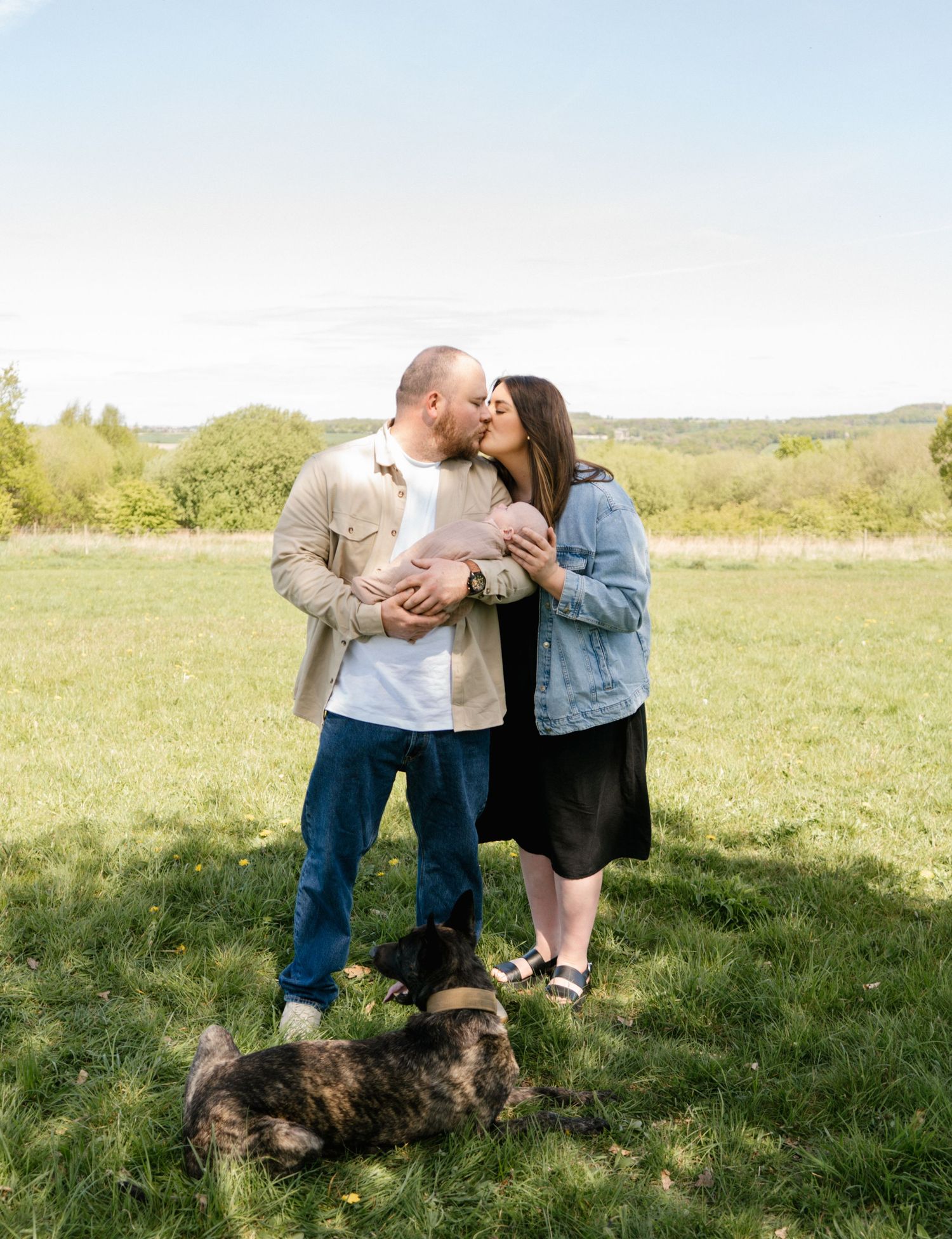 A couple shares an intimate moment while standing together in a grassy field on a sunny day.