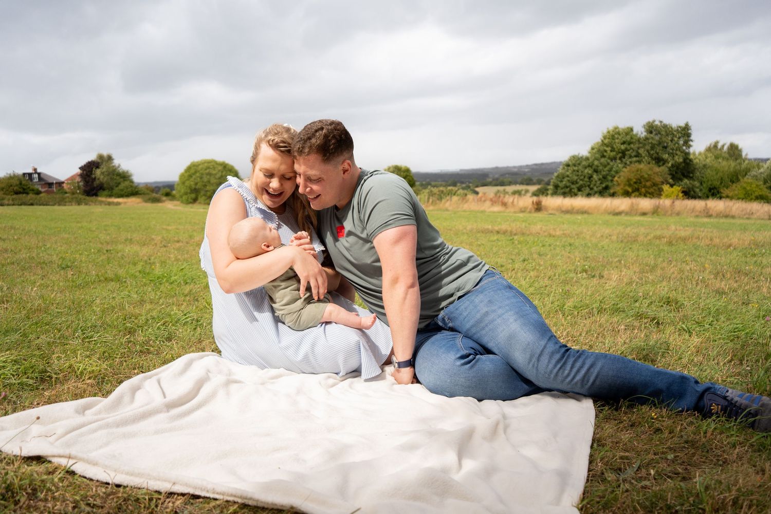 Family relaxing together on a blanket in a peaceful meadow setting.