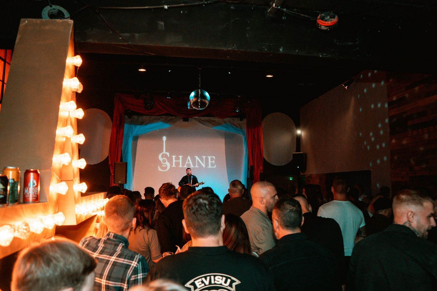 Music venue interior with orange stage lights and projected text on screen.