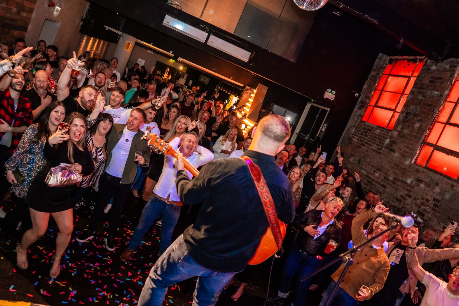 Packed dance floor with enthusiastic crowd enjoying live music under dramatic lighting.