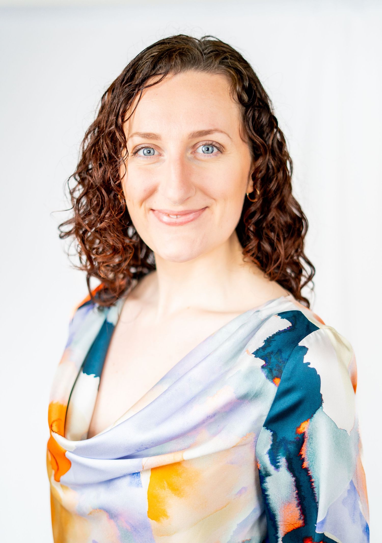 Professional portrait of someone in a colorful artistic scarf against white background.