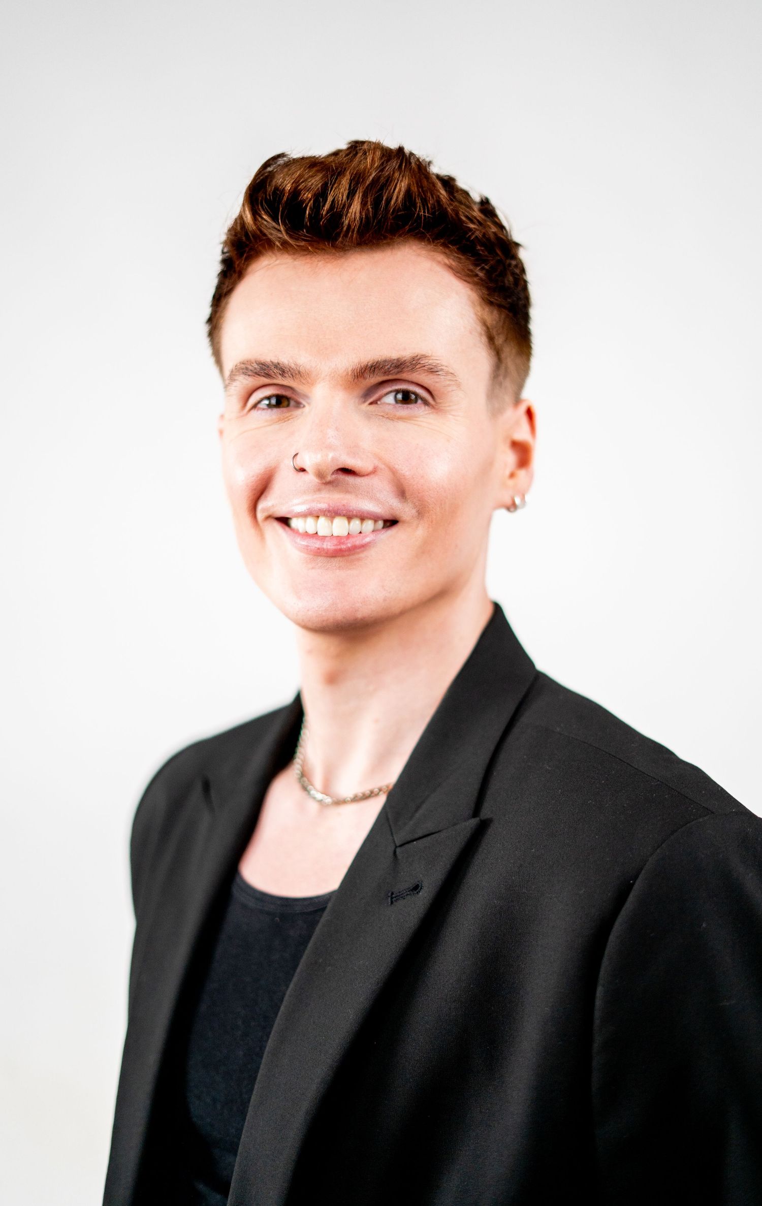 Professional headshot of a person in a black blazer smiling warmly against a light background.