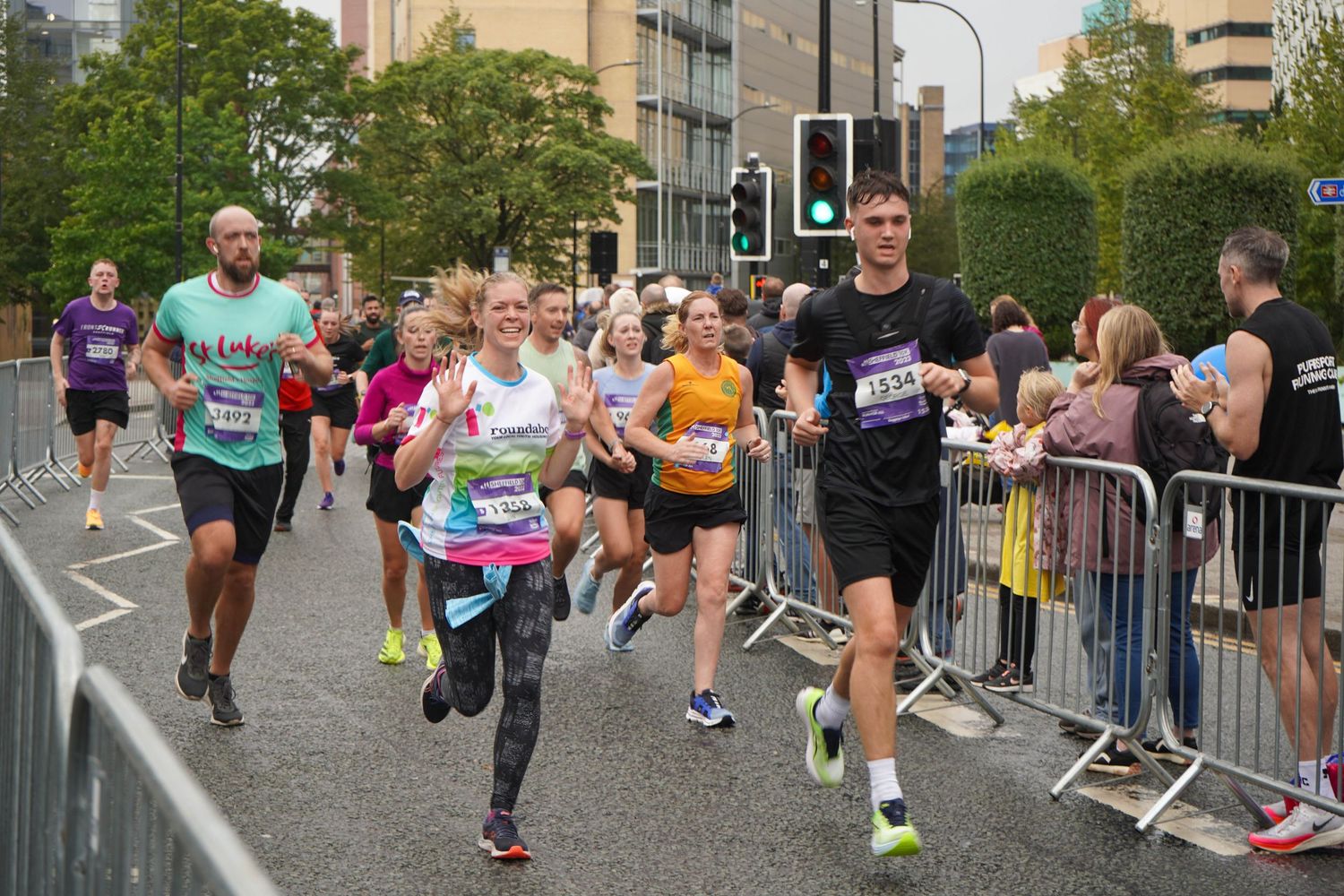 Crowd of runners competing in an urban marathon with spectators behind barriers.
