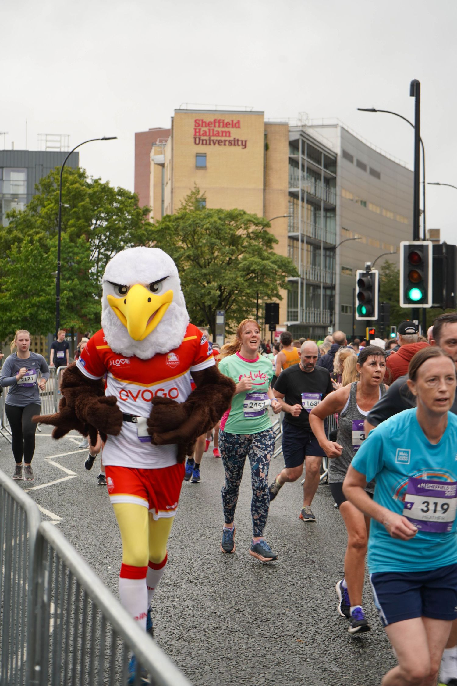 Race participants running alongside a mascot in an eagle costume during a community event.