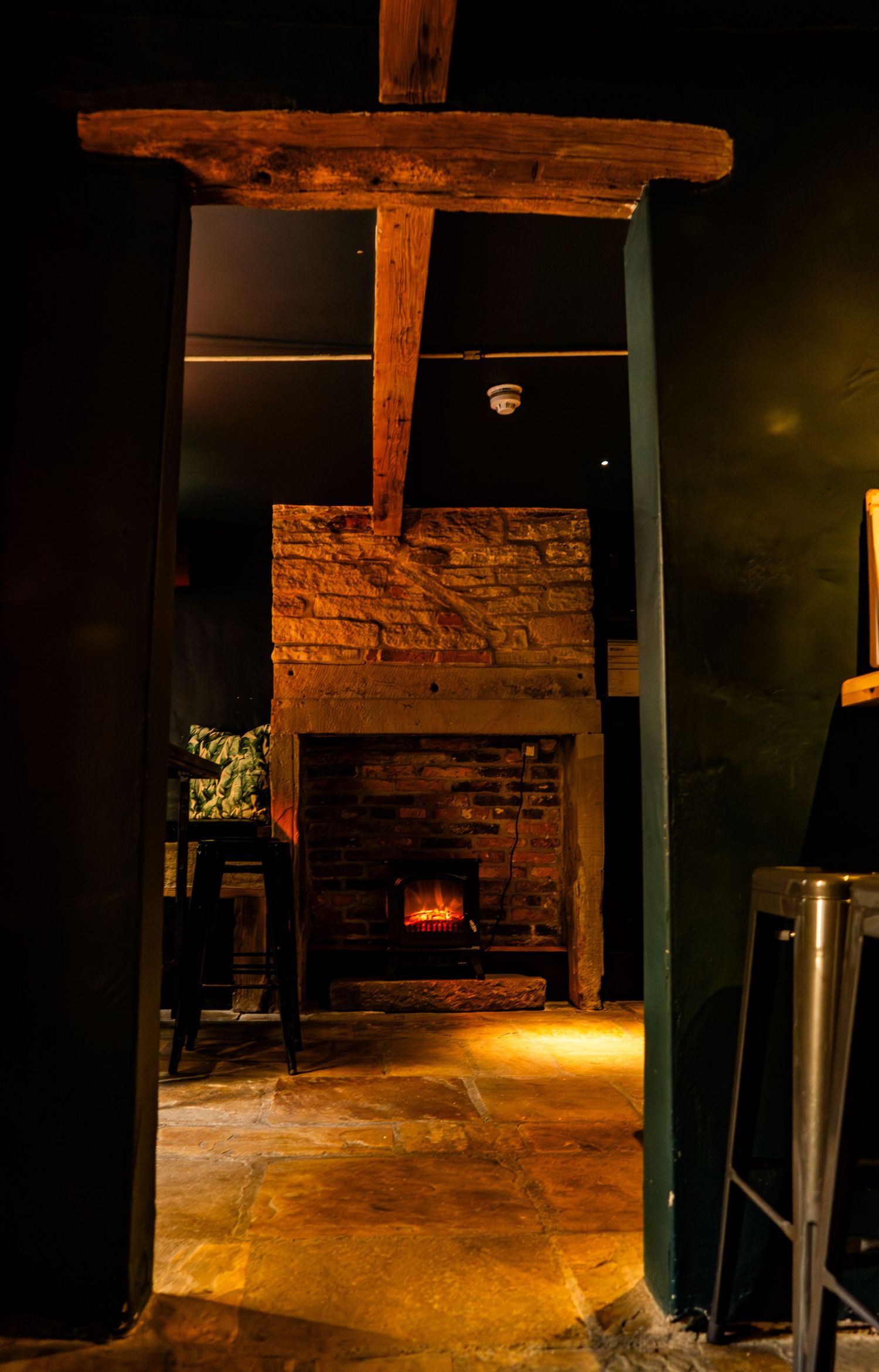 Rustic wooden doorway frames a cozy brick fireplace with warm ambient lighting.