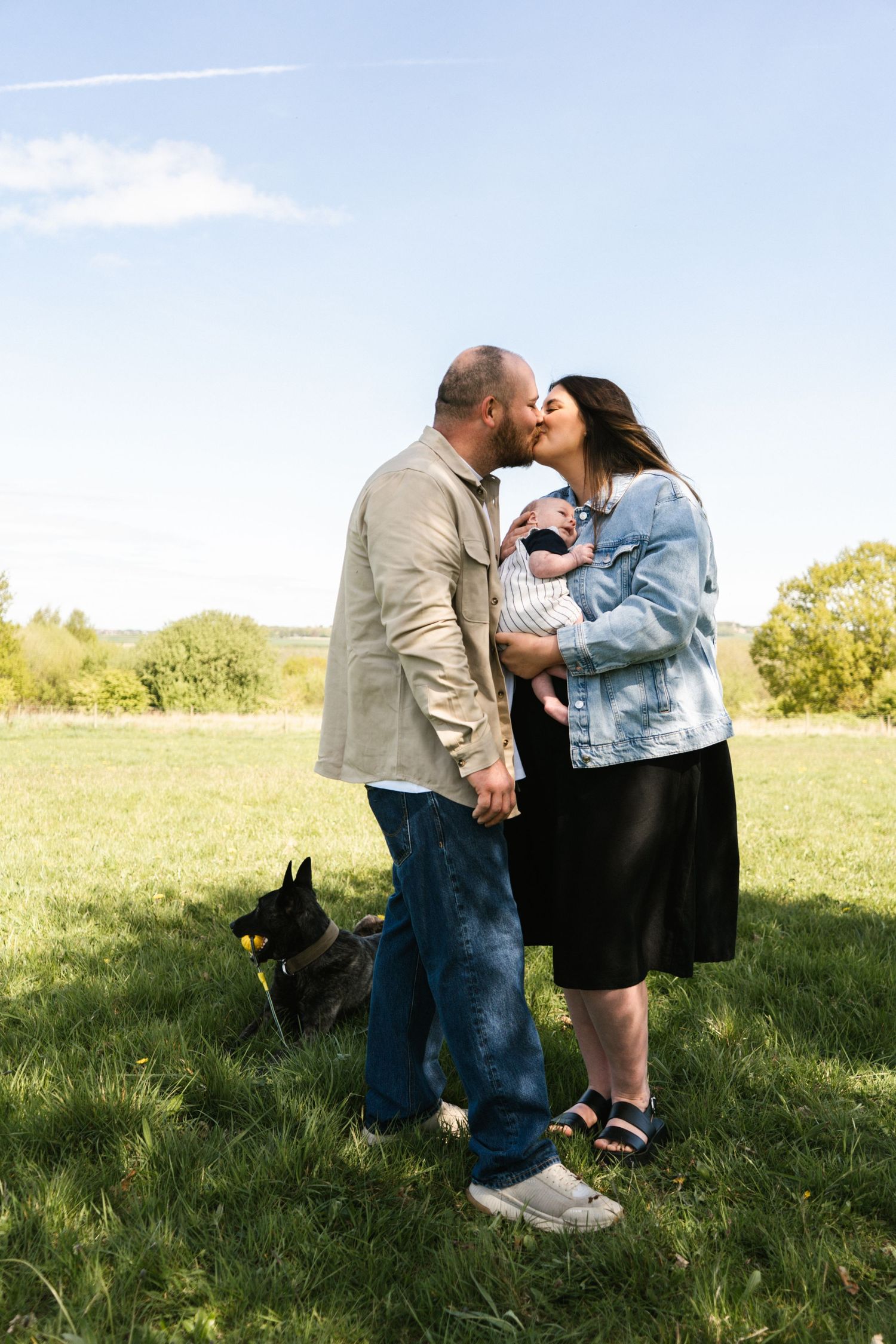 Family moment in a green field with their dog on a bright sunny day.