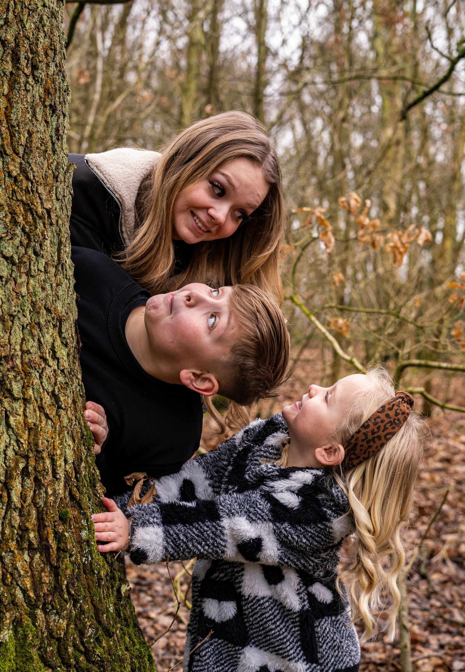 Joyful interaction between family members playing around a mossy tree trunk.