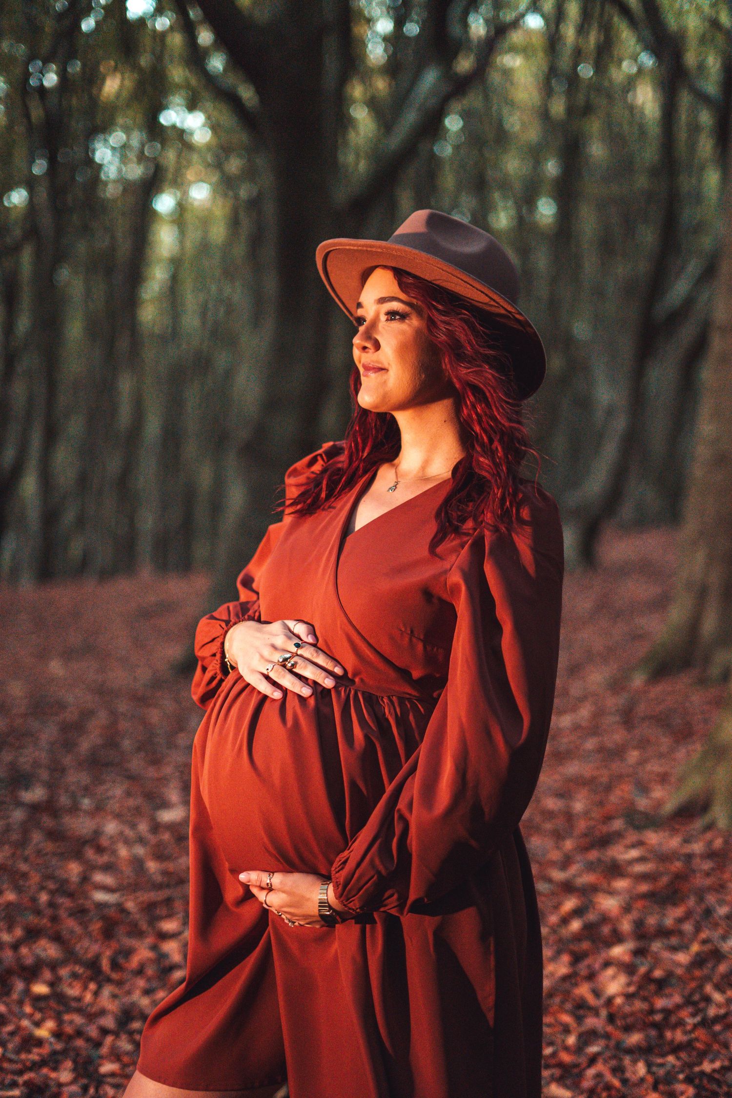 Person in vintage red dress and hat stands among fallen autumn leaves in forest.