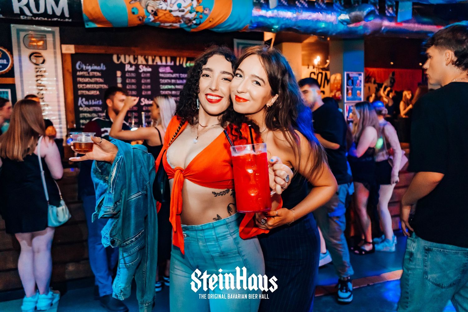 Bar patrons mingling and dancing under colorful nightclub lights.