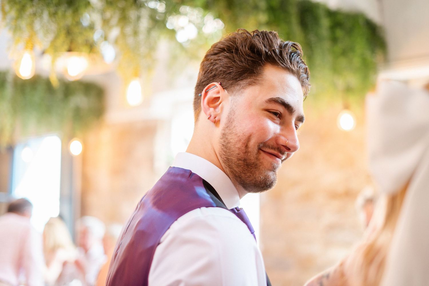 Wedding guests celebrate during an outdoor reception with string lights and greenery decorations.