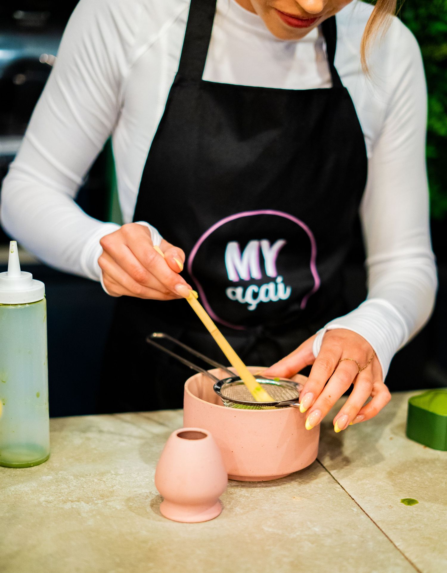 Hands preparing food in pink ceramic bowls on a concrete countertop.