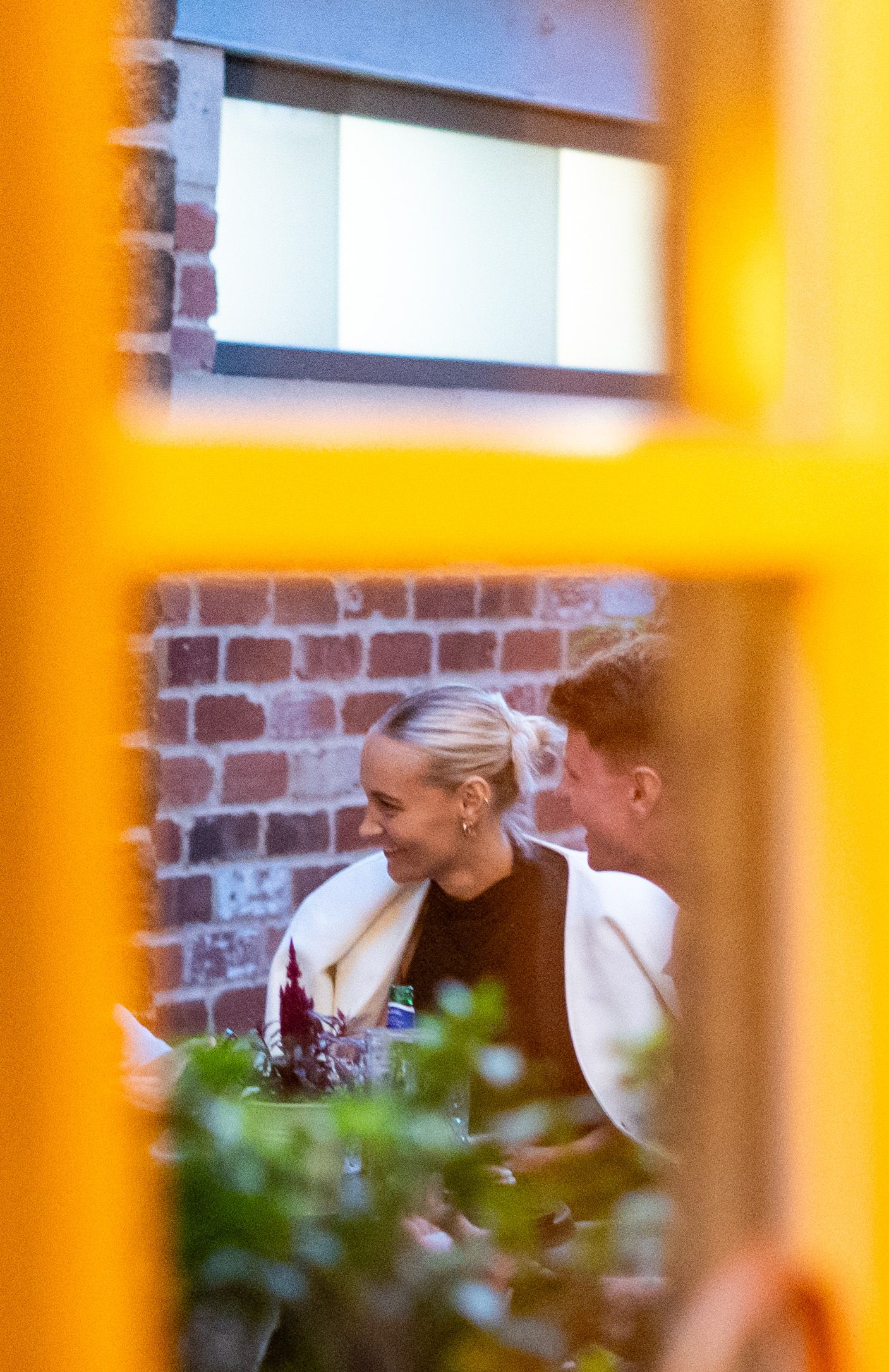 A candid moment captured through window frames with warm orange lighting.