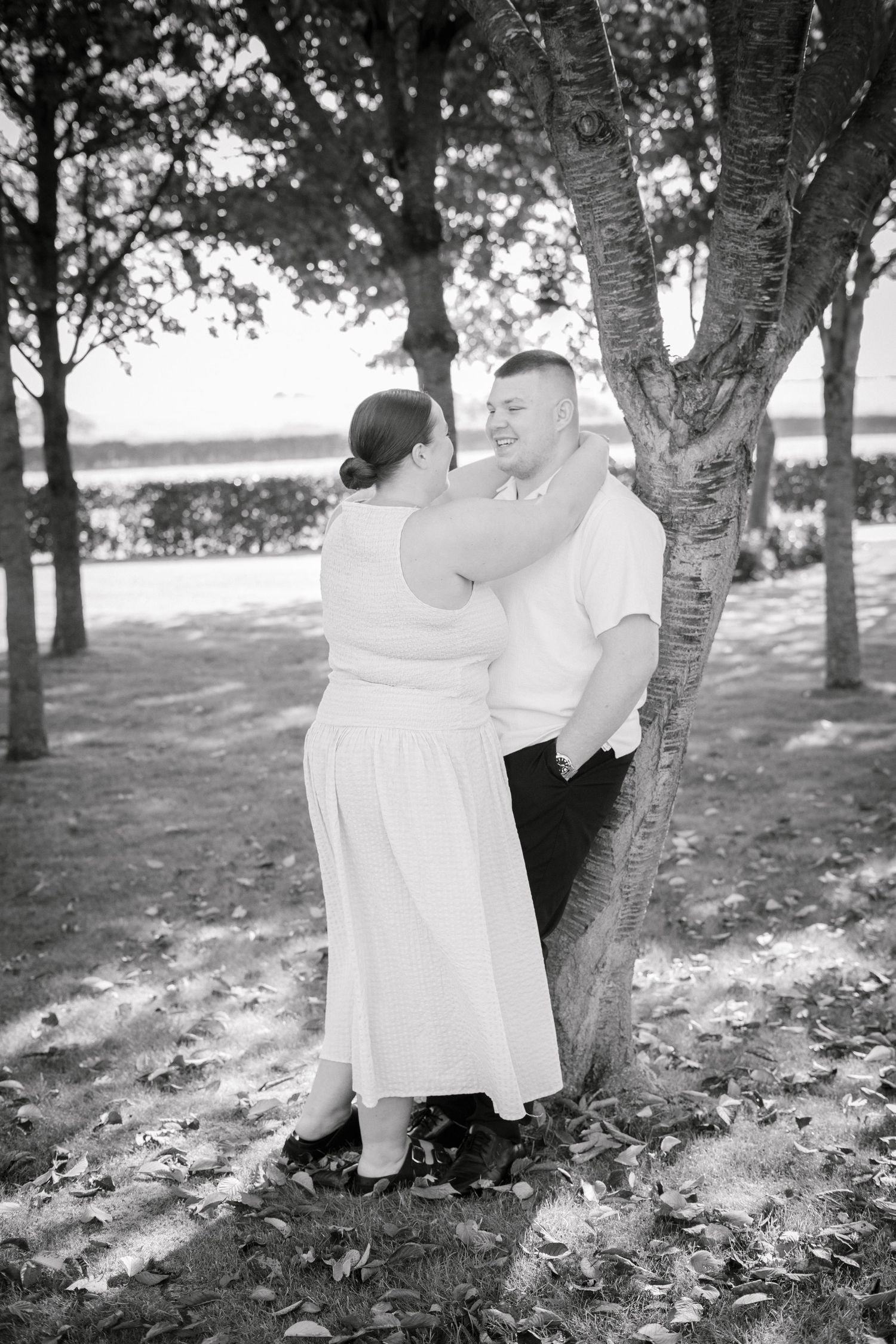 Black and white photo of figures in white dress and dark suit by birch trees in autumn.