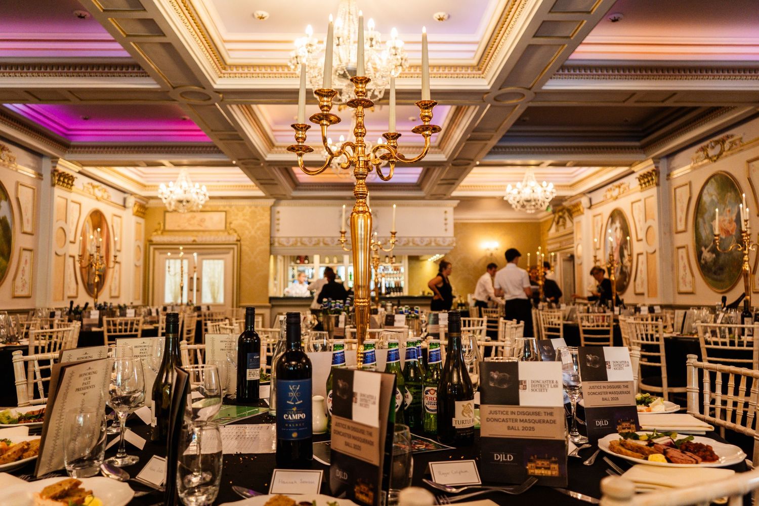 Elegant ballroom with ornate chandeliers and coffered ceiling set for formal dinner event.
