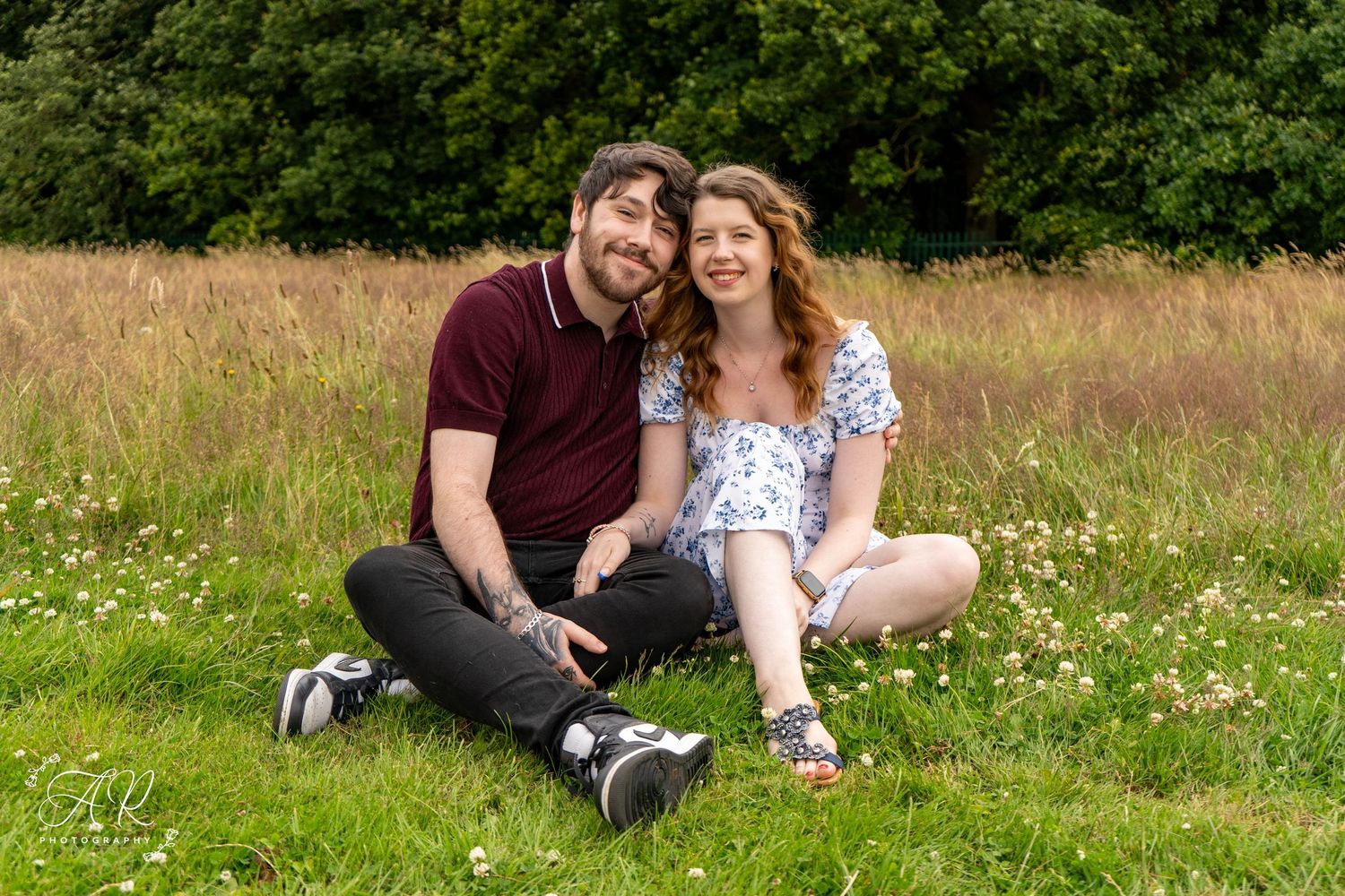 A couple sits together in a blooming meadow surrounded by wildflowers and greenery.