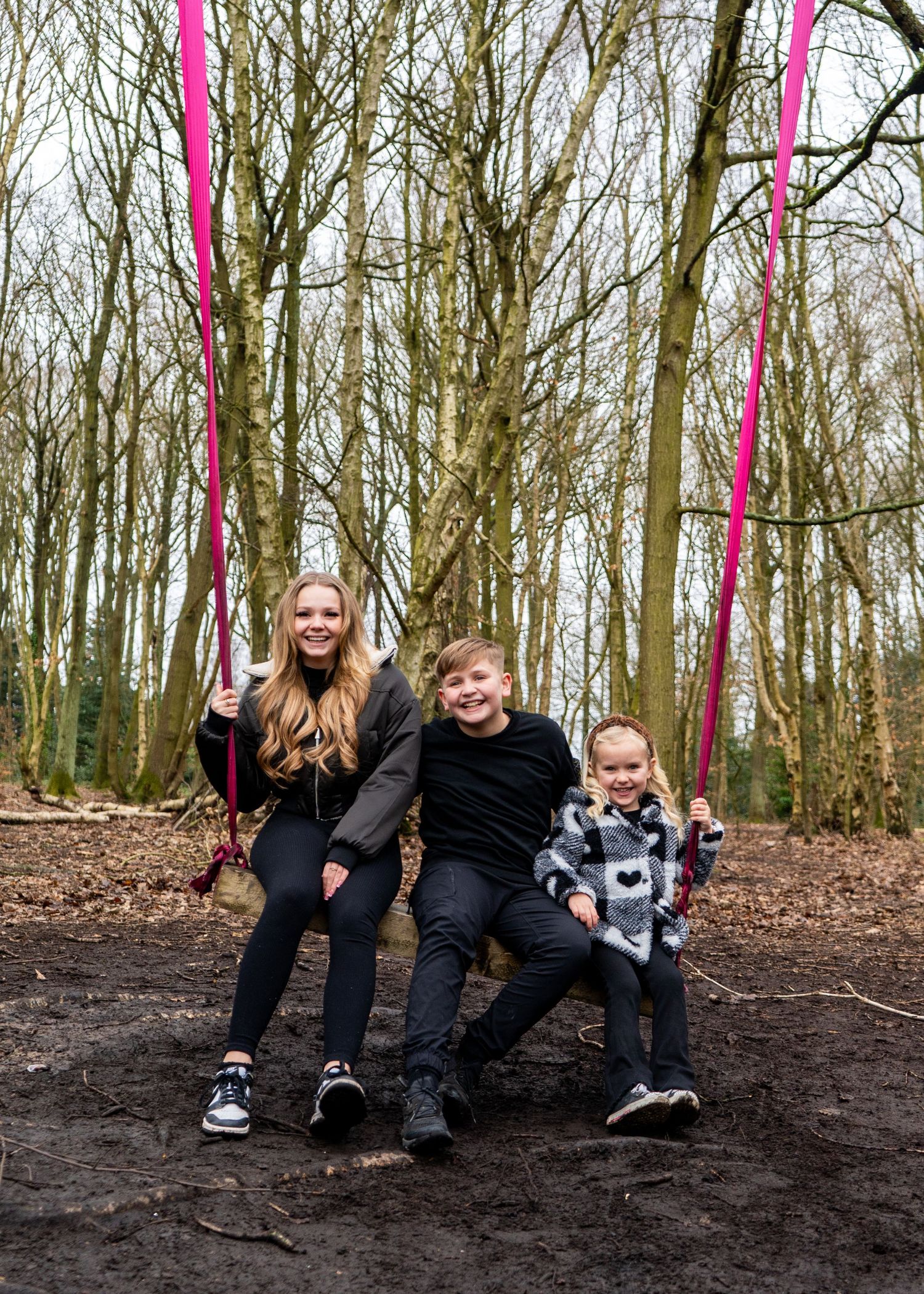 A candid family moment captured on a dirt embankment in a wooded area with pink ribbons.