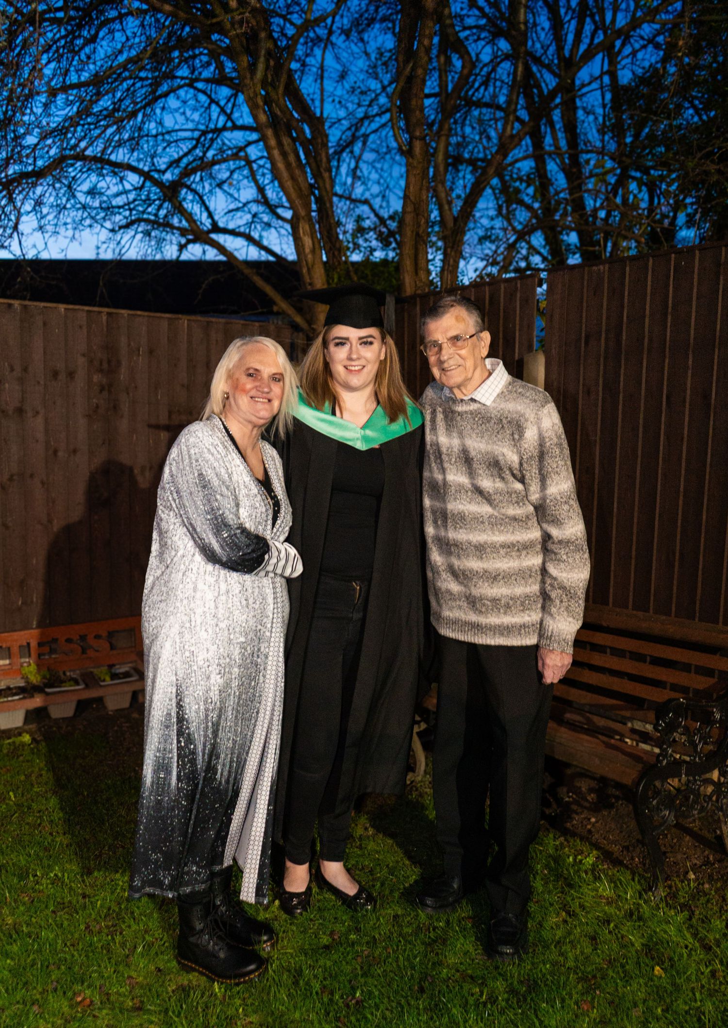 Family members pose together outdoors during a graduation celebration with trees in background.