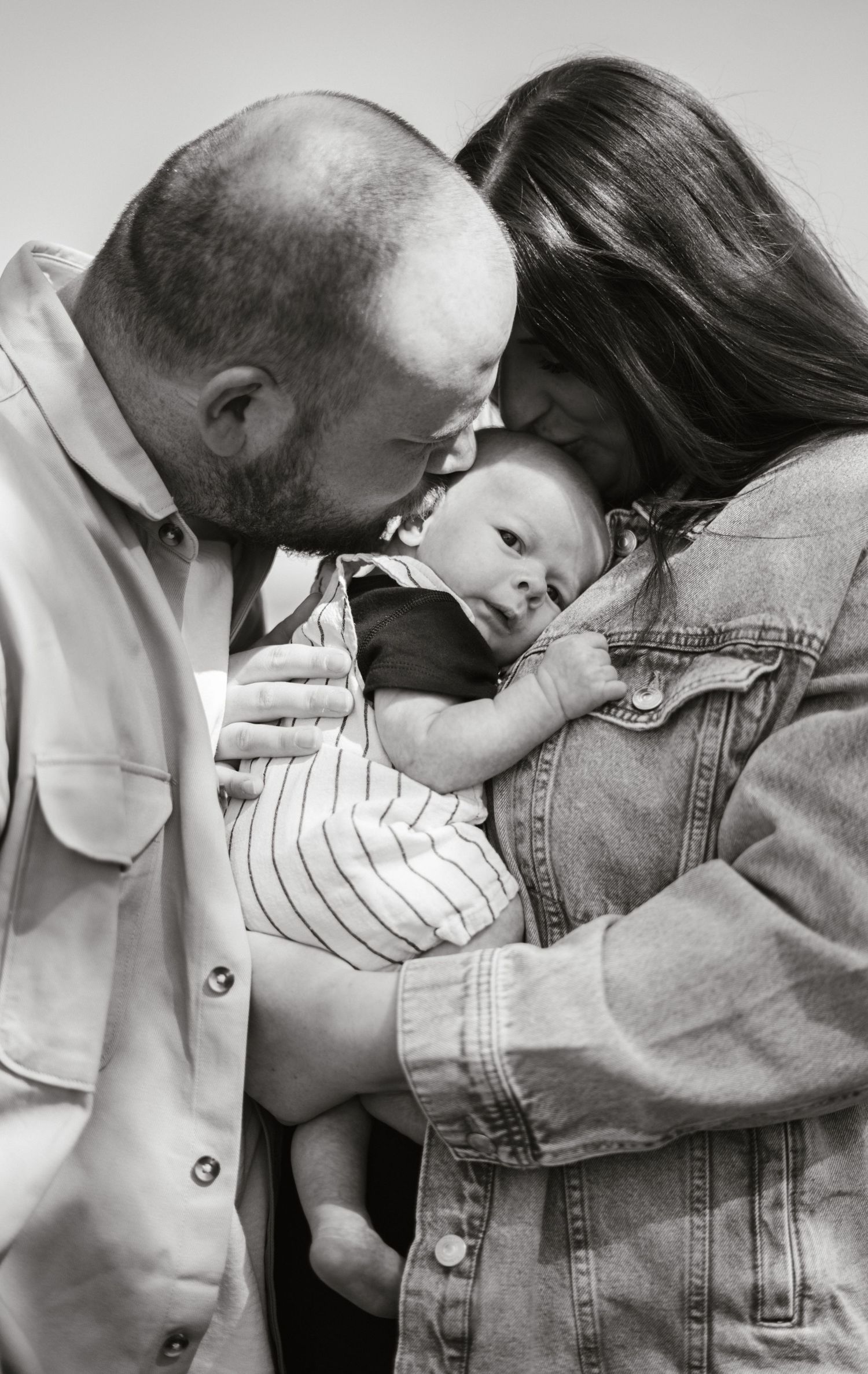Black and white intimate portrait of parents sharing a tender moment with their baby.