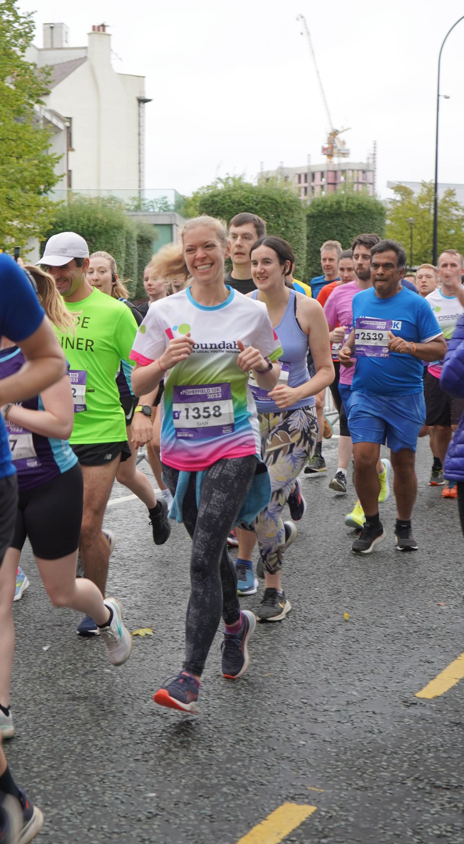 Large group of runners participating in a charity race on a wet city street.