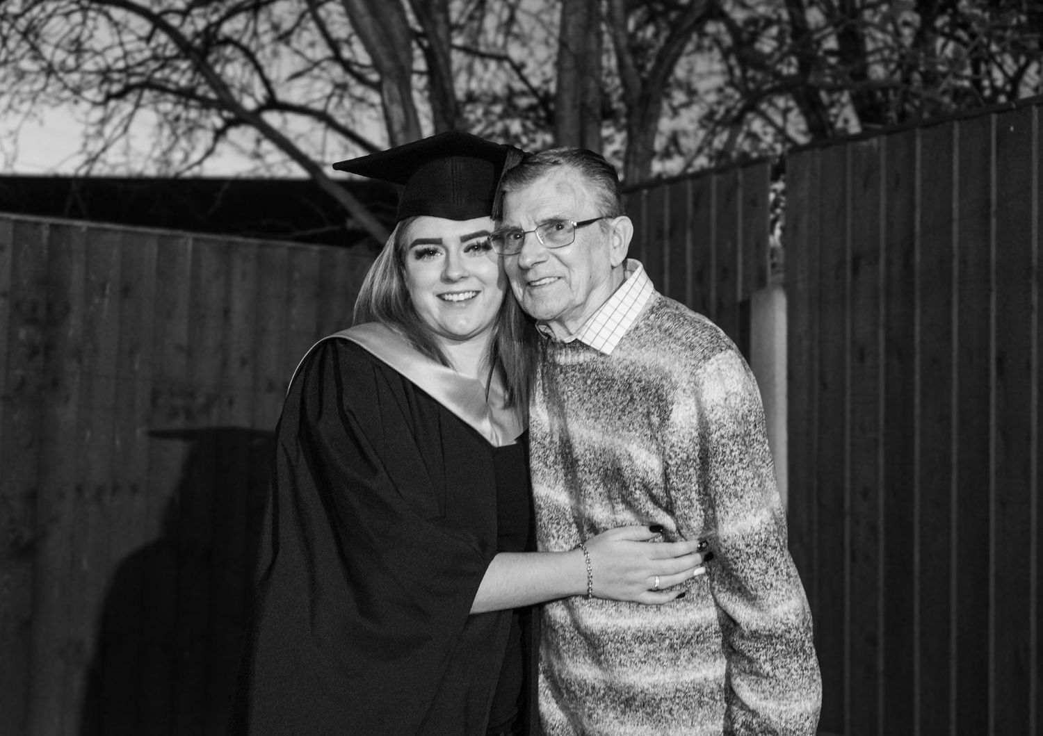 A graduation celebration photo session in front of a wooden fence at dusk.