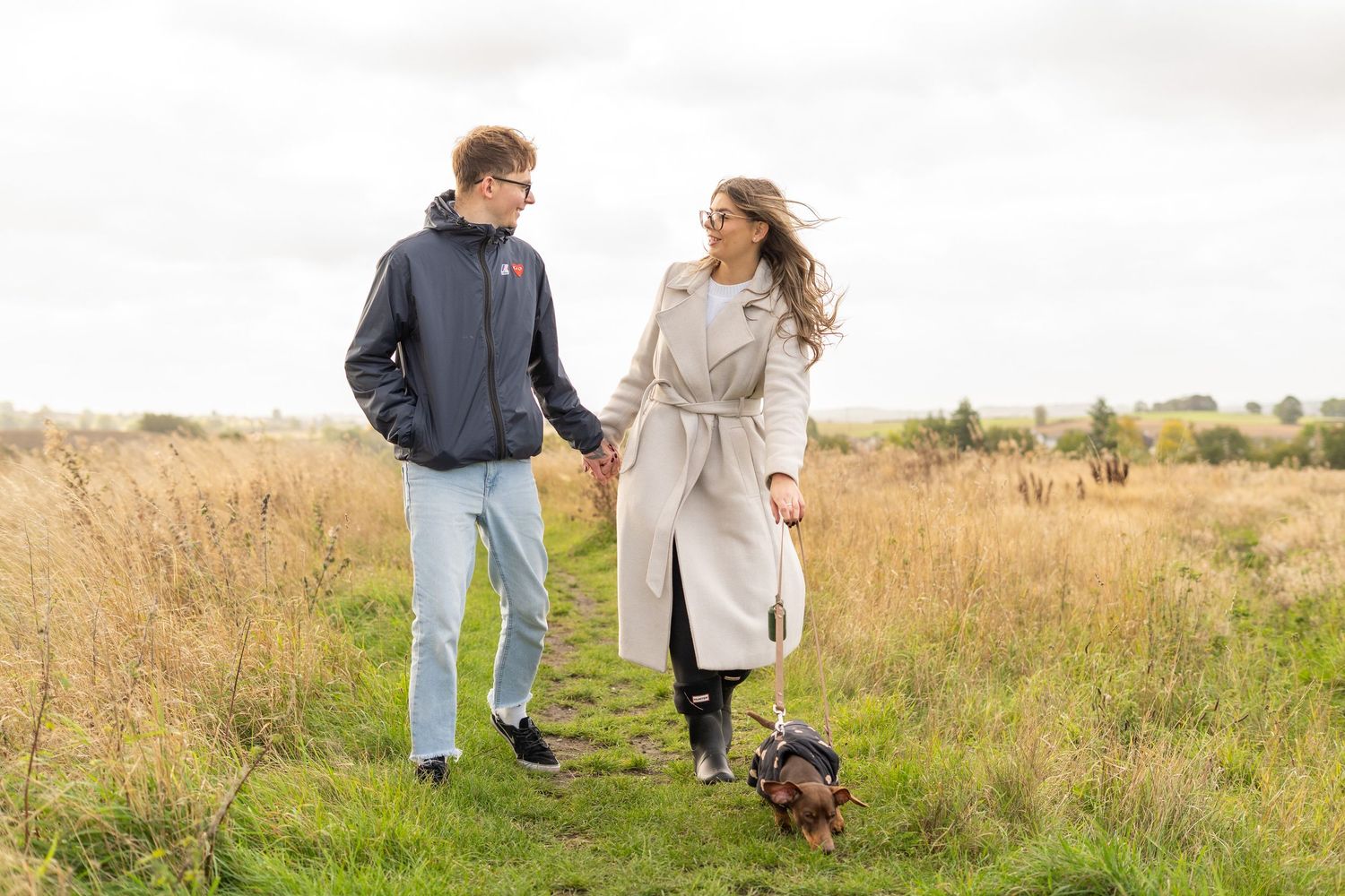 Couple enjoying an autumn walk with their dachshund in a rustic field setting.