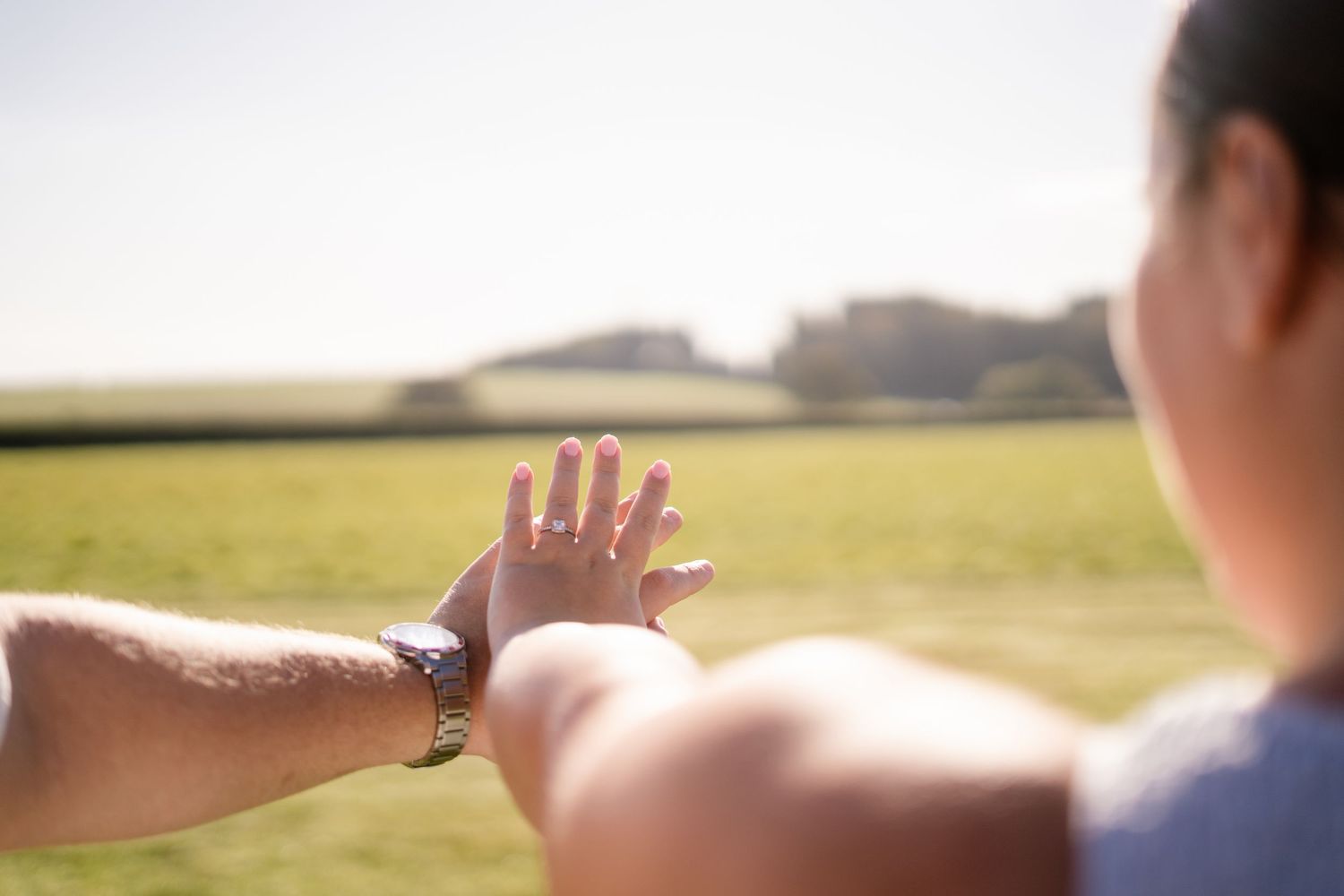 Two hands reaching towards each other against a sunny field background.