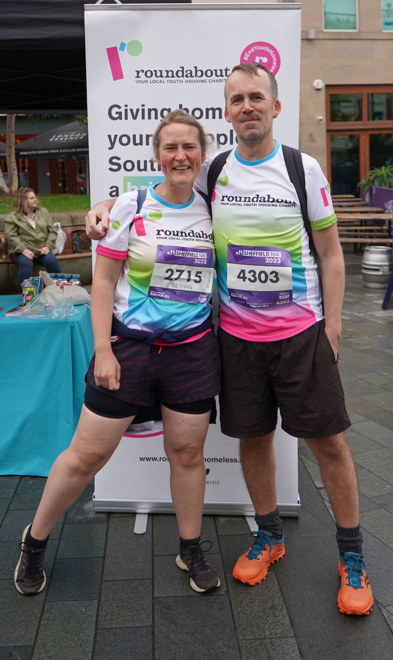 Runners wearing race bibs and colorful shirts pose in front of Roundabout charity banners.