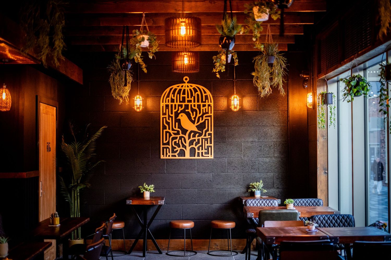 Restaurant dining area with modern decor featuring dark walls, wooden tables and decorative bird cage art.
