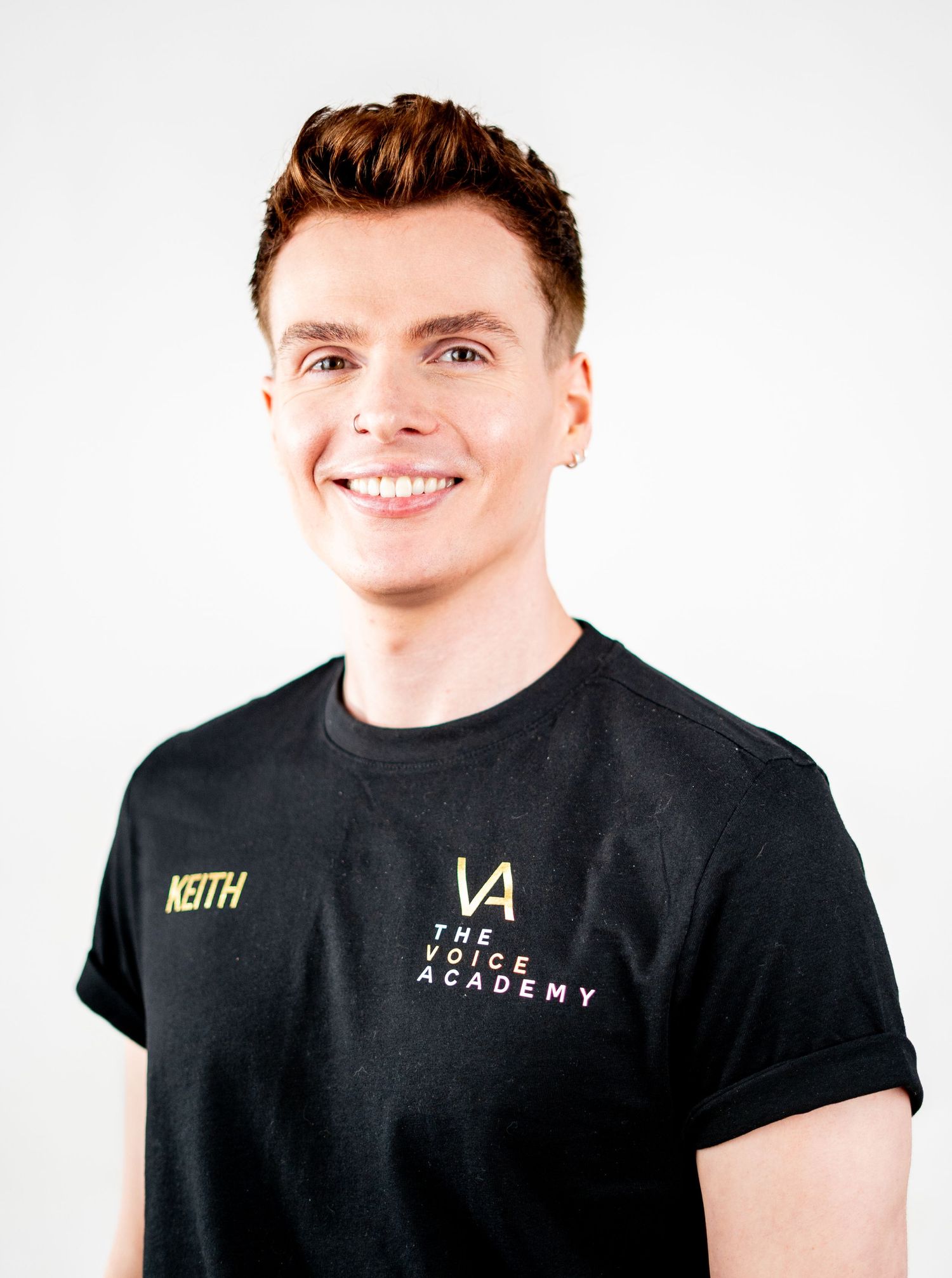 Professional headshot of a person in a black branded t-shirt with short styled hair.