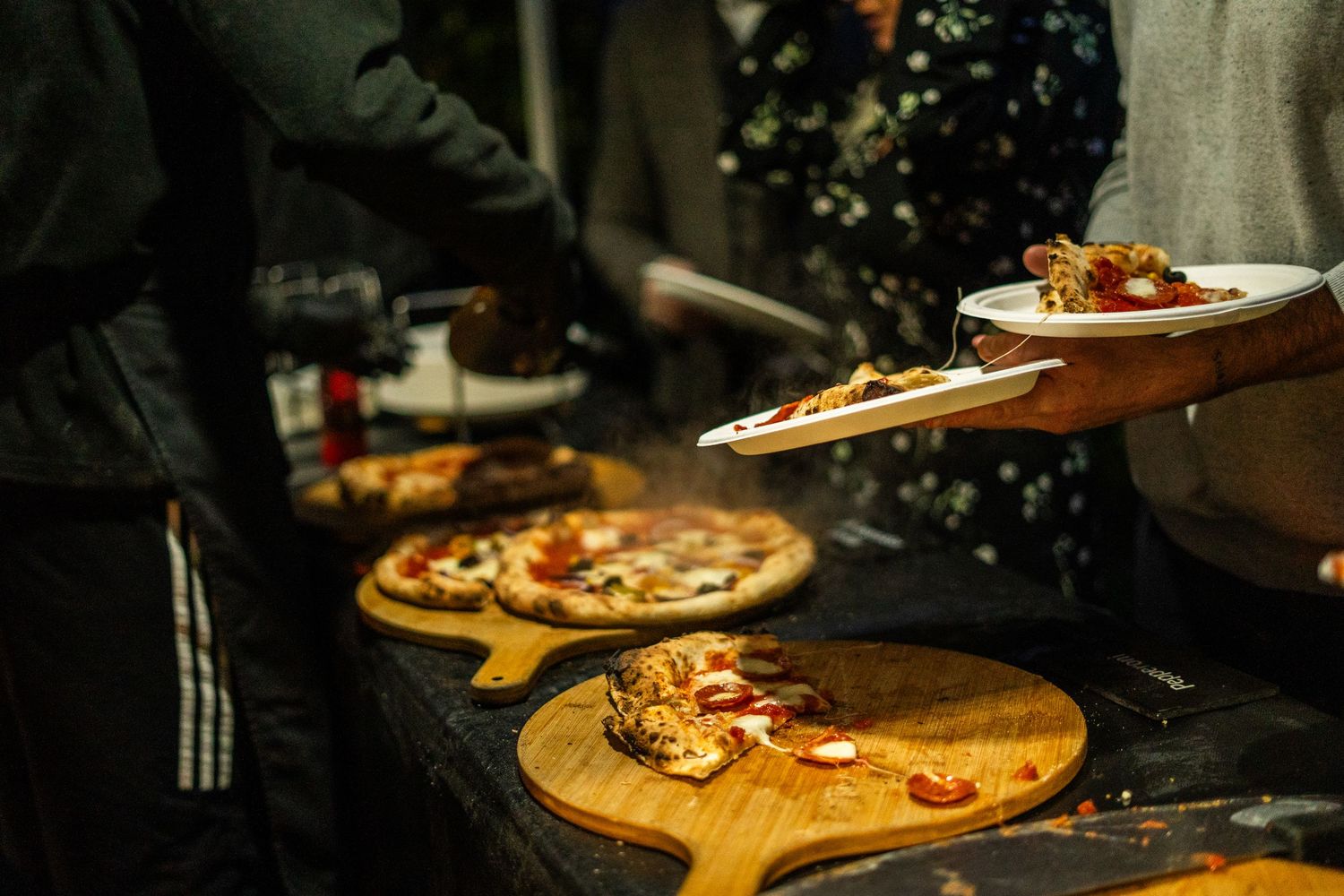 Multiple pizzas on wooden serving boards being plated at a catering station.