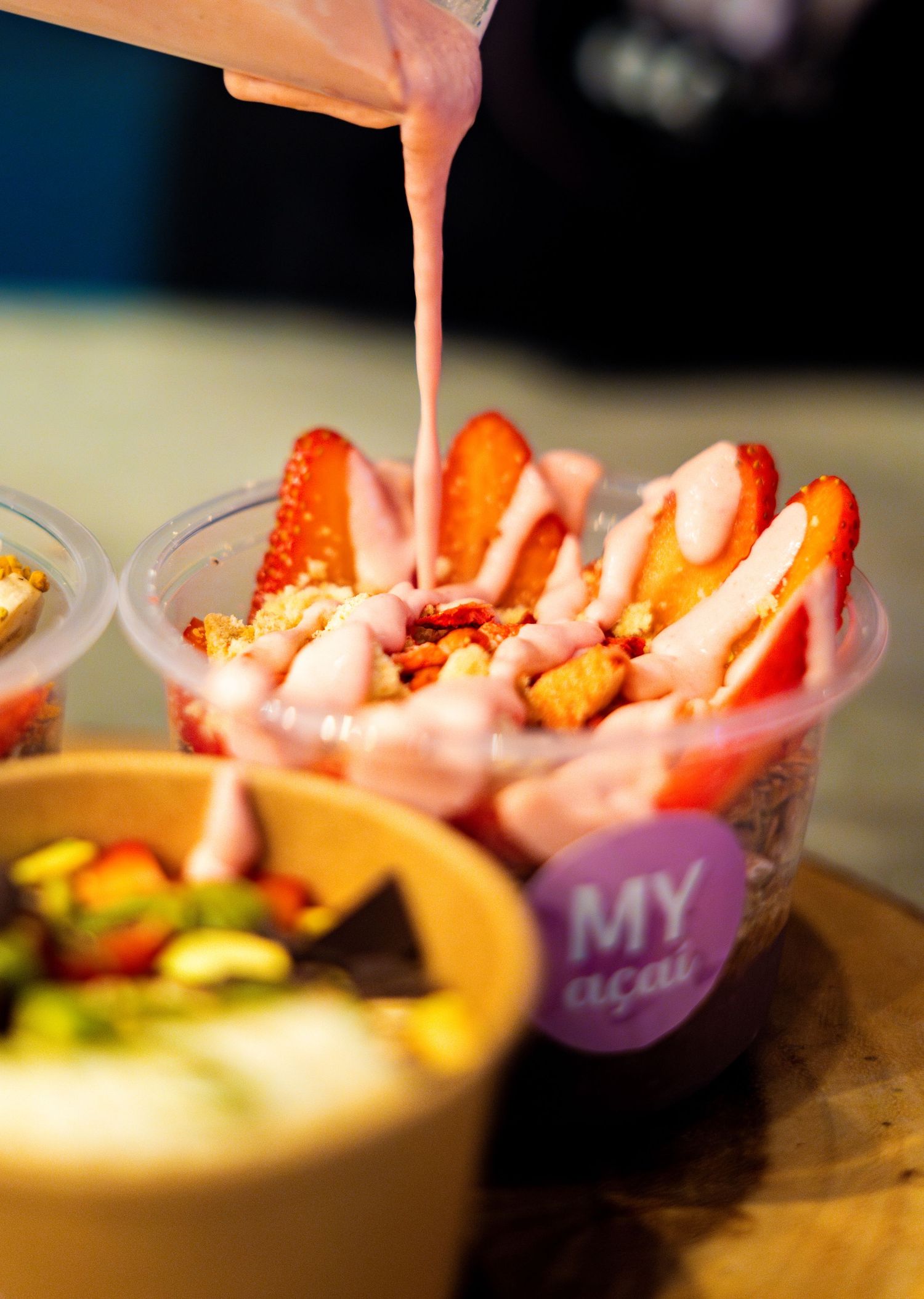 Fresh strawberries being topped with pink sauce in an acai bowl.