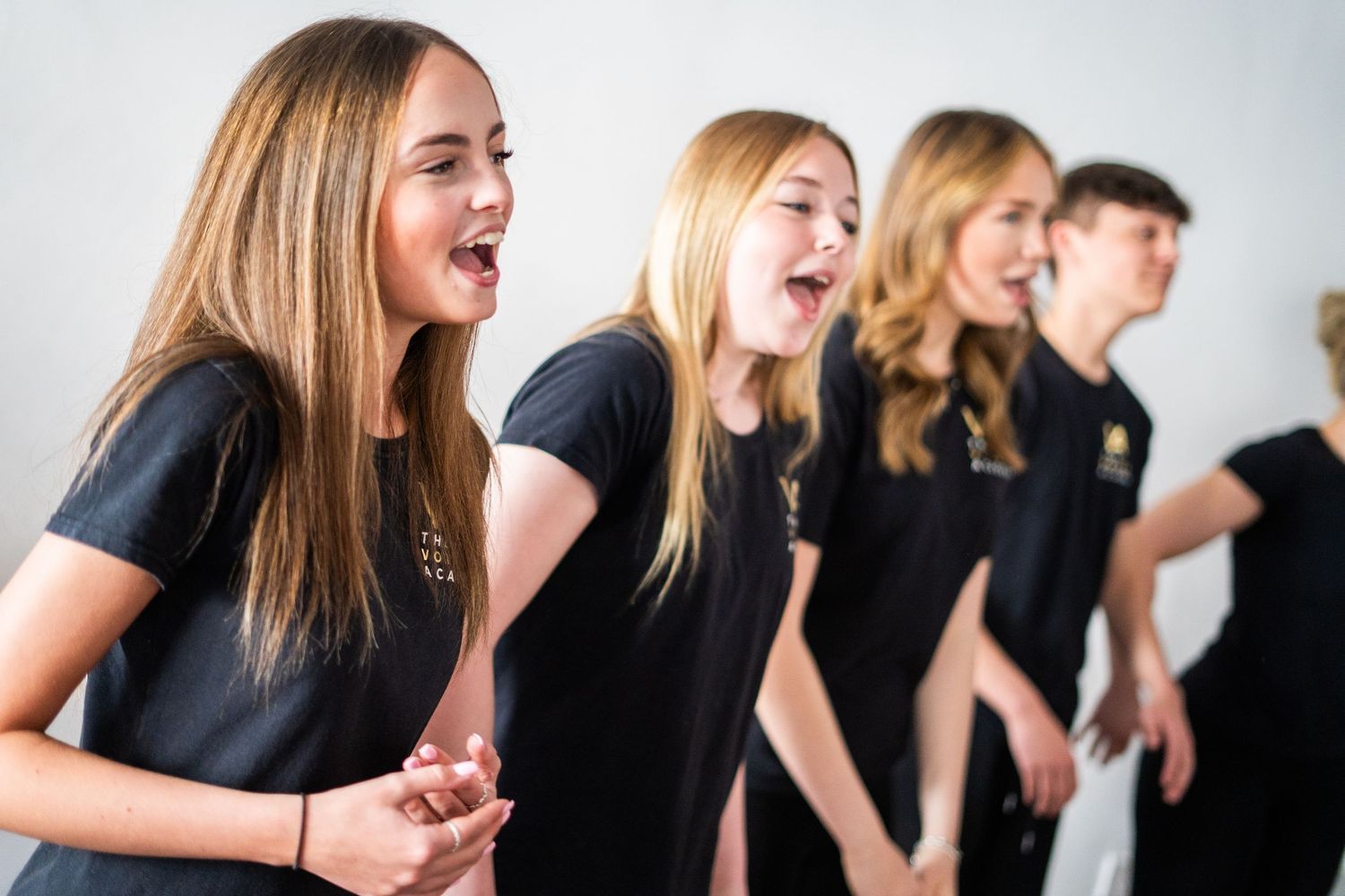 Group of performers in black uniforms singing together during rehearsal.