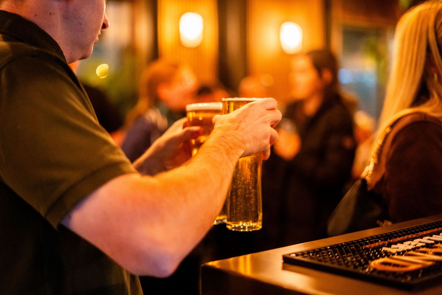 Bartender serving draft beer at busy bar counter with warm ambient lighting.