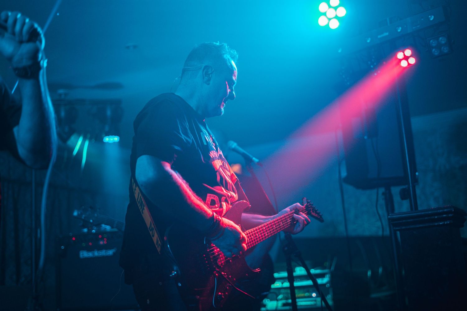 Guitarist performs on stage under dramatic blue and red lighting during a concert performance.