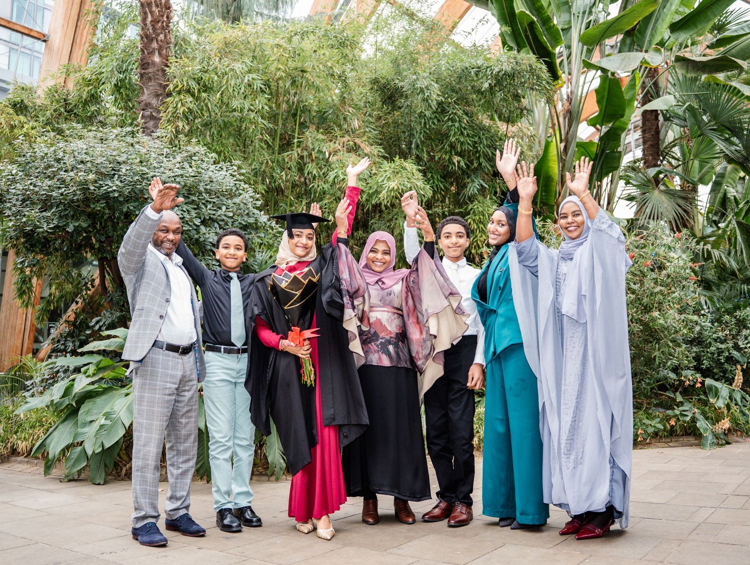 Graduates gather for a group photo in a garden setting wearing academic regalia.
