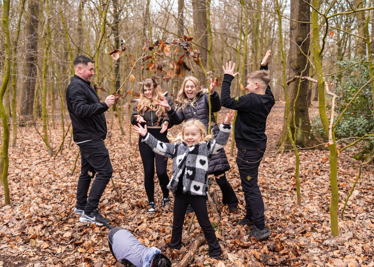 Playful family throwing autumn leaves in wooded area during photo session.