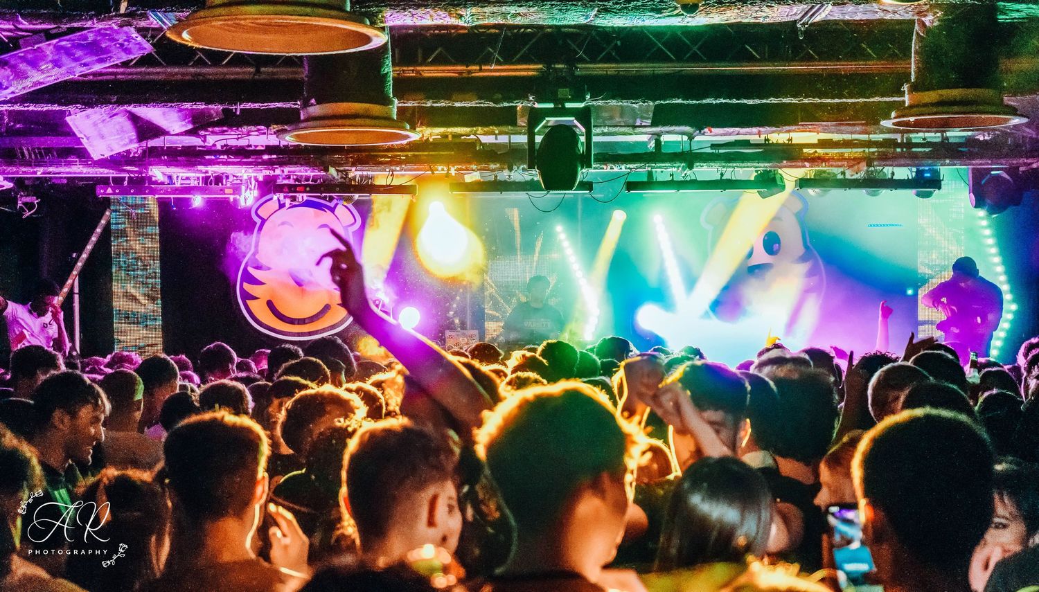 Silhouetted crowd at a nightclub under colorful rainbow lighting effects.
