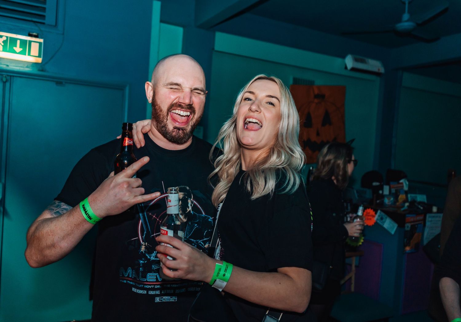 People laughing and socializing at a nightclub with teal-colored lighting.