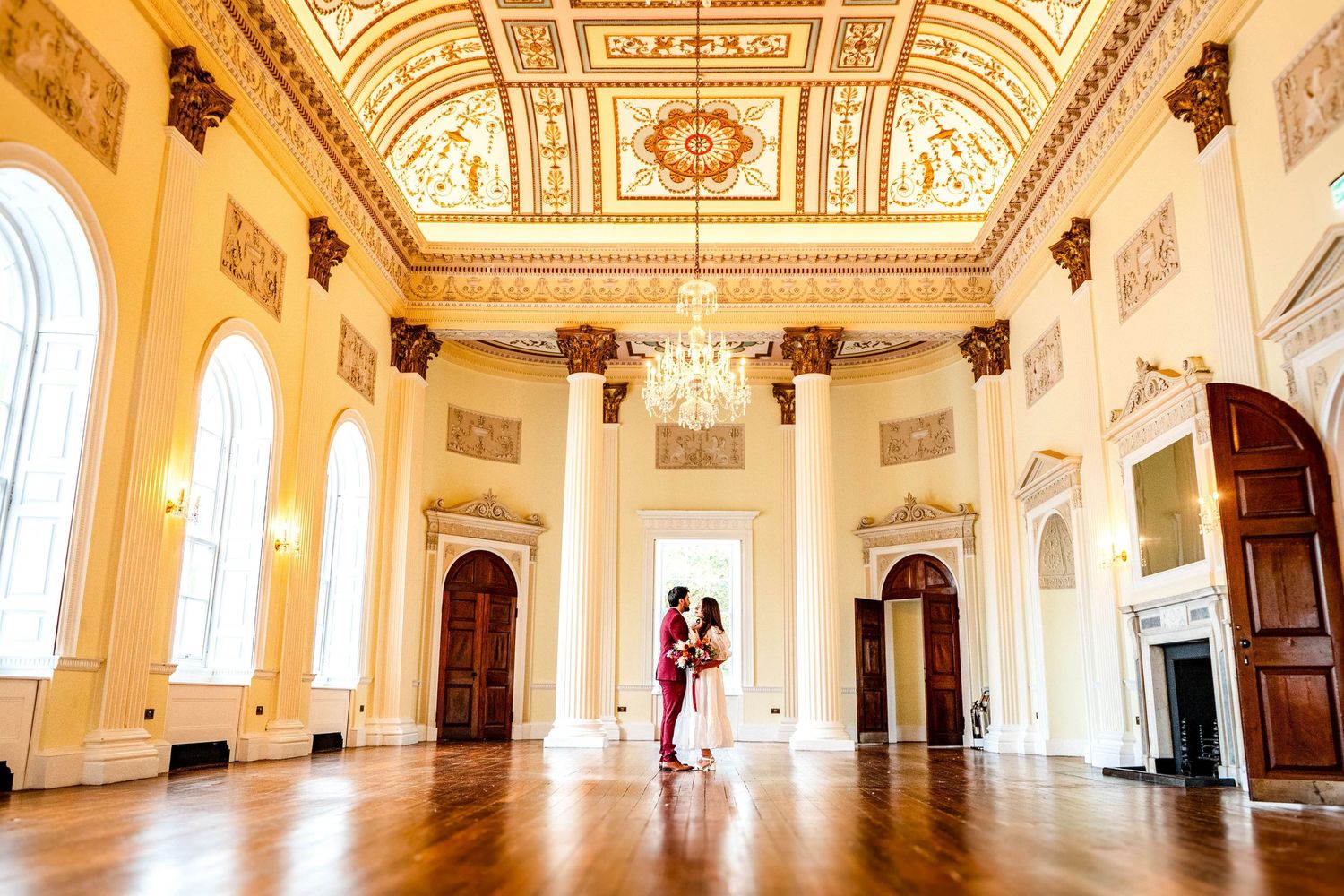 Ornate ballroom interior with gilded ceiling details and crystal chandeliers in a historic building.