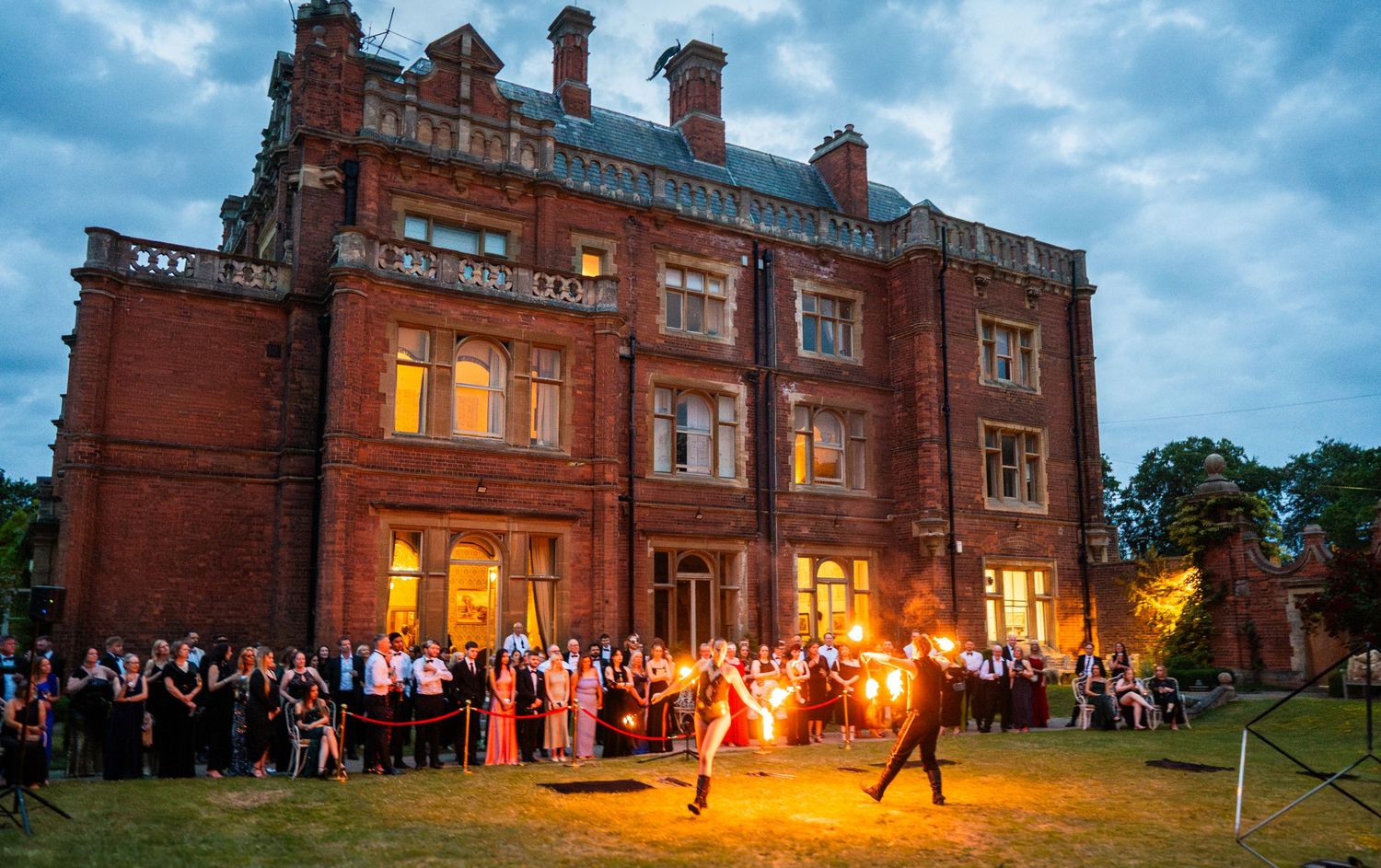 Panoramic view of a grand red brick mansion lit up at dusk during a wedding celebration.