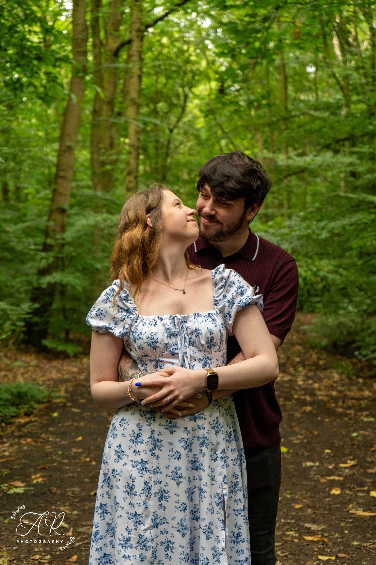 A couple shares an intimate moment on a forest trail surrounded by greenery.